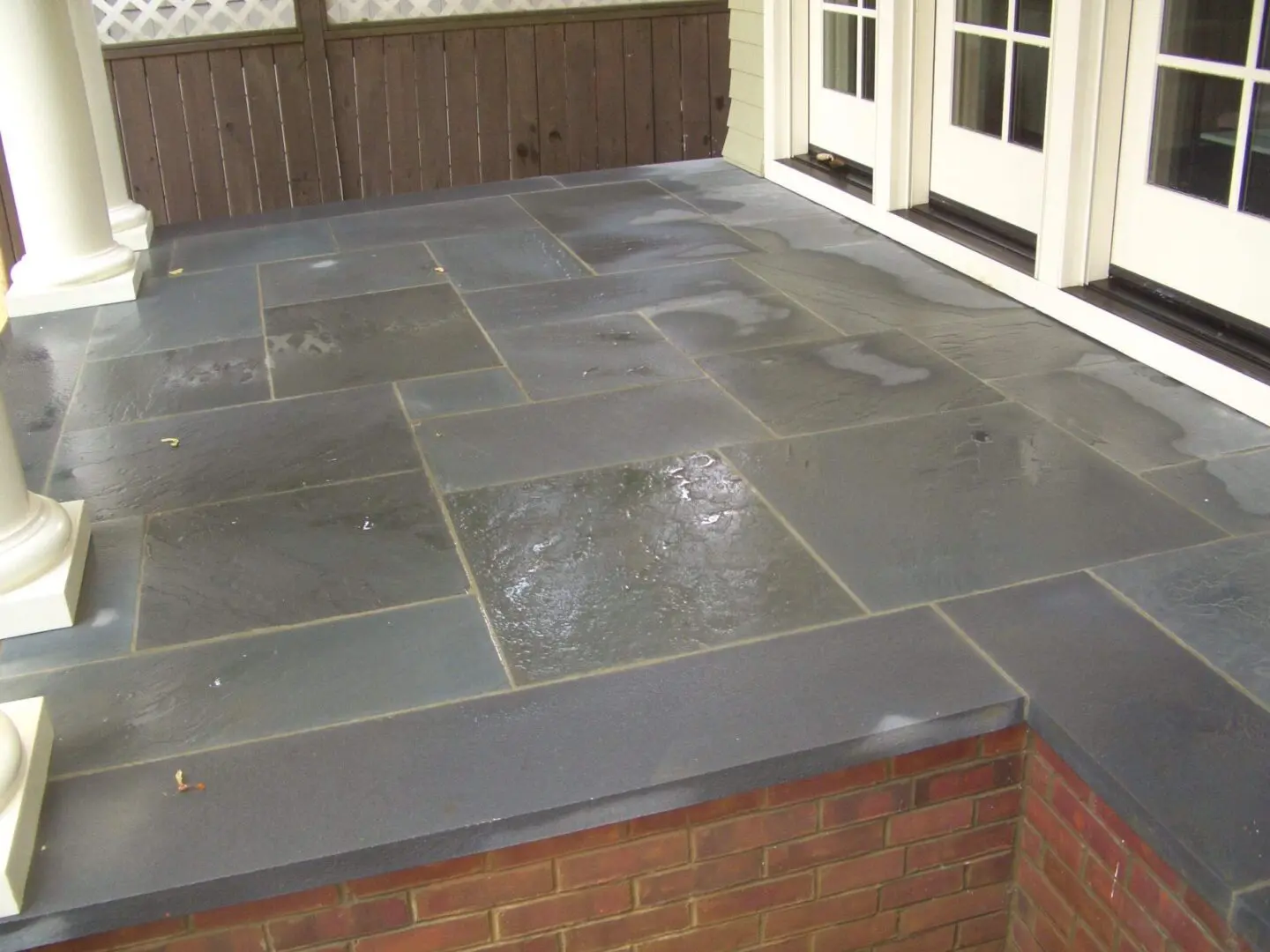 A clean, wet stone patio with rectangular tiles outside a house.