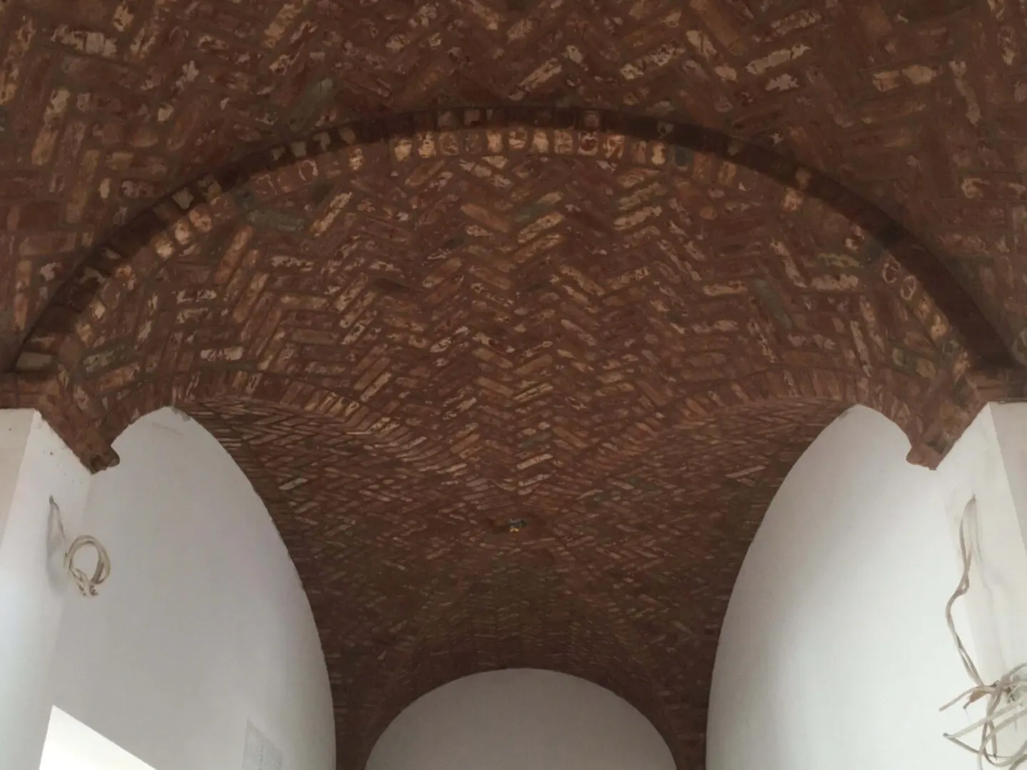 Curved brick ceiling with white, smooth, egg-shaped sculptures beneath.