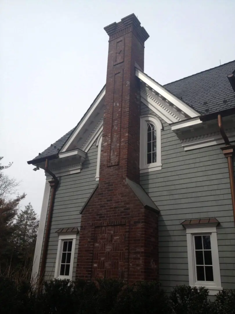Tall brick chimney attached to a gray wooden house.