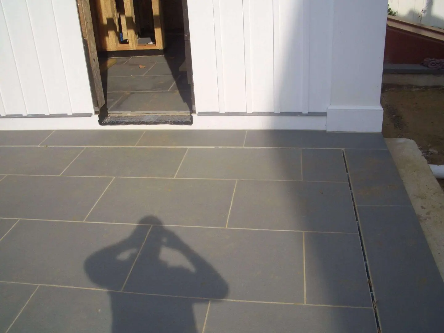 Shadow of a person taking a photo on a tiled floor outside a door.
