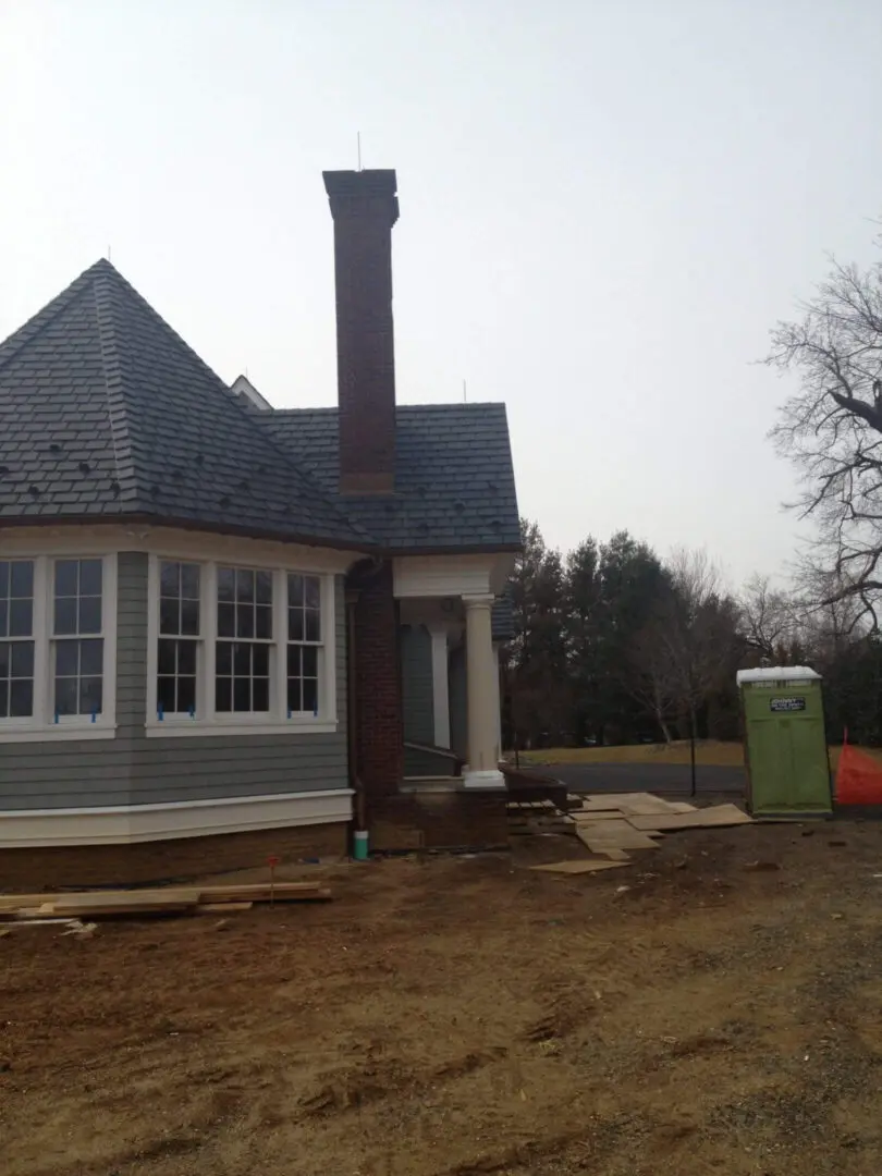 A house exterior with a chimney and portable toilet on a cloudy day.