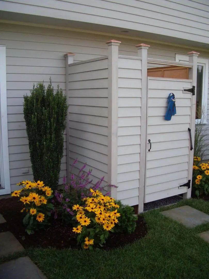 Outdoor garden shower with white wooden panels and colorful flowers.