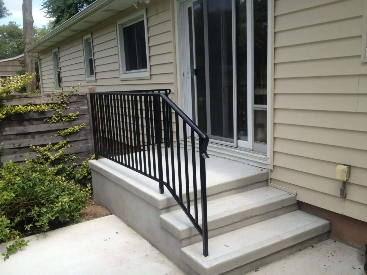 Black metal handrail on concrete porch steps outside a house.