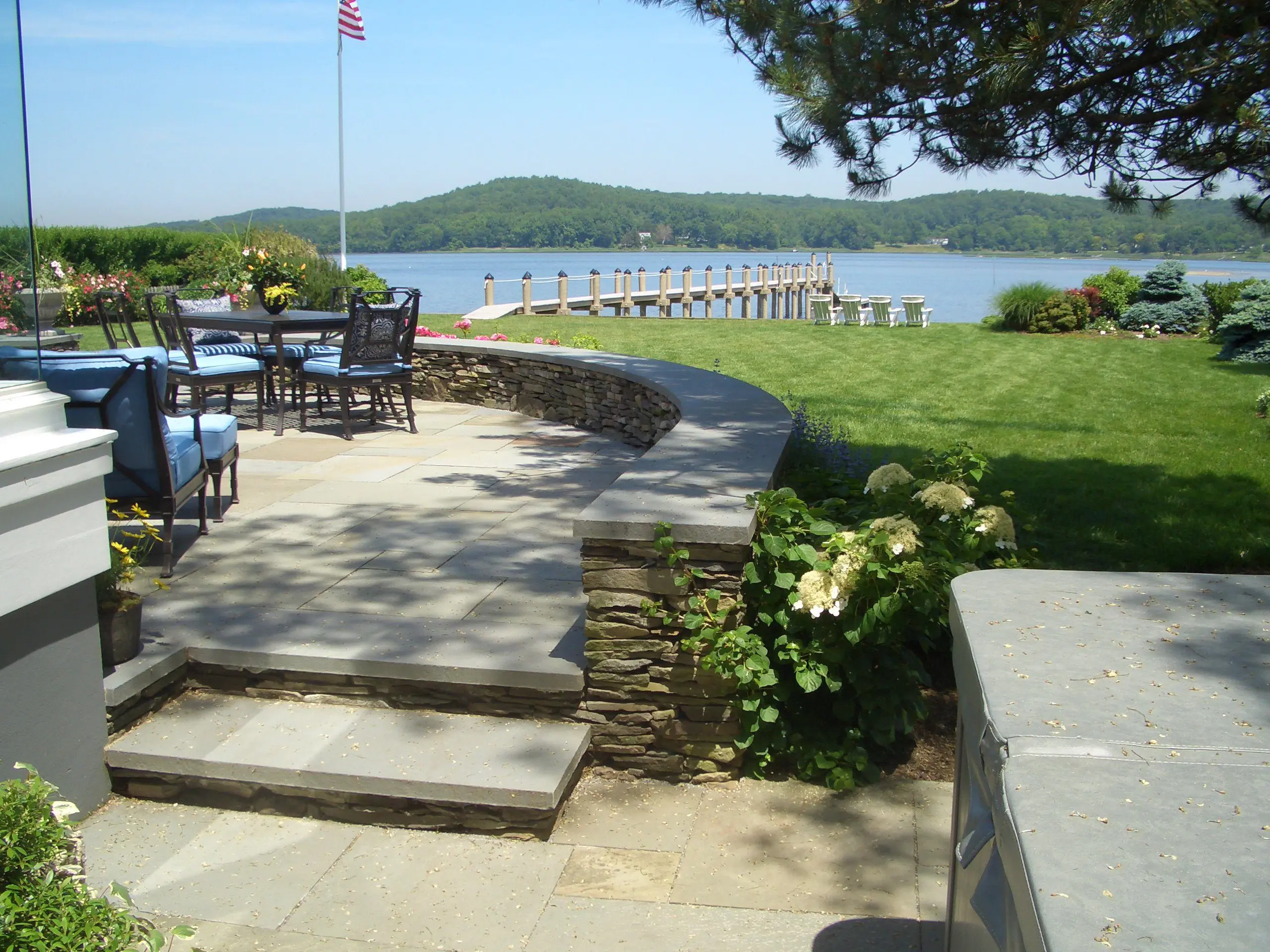 Outdoor seating area by a lake with a dock and greenery.