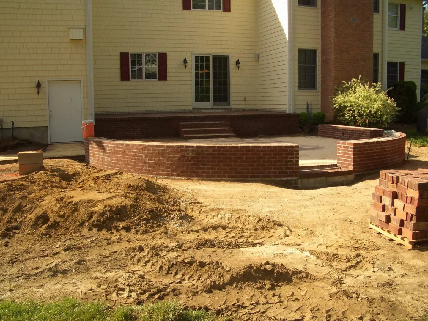 Newly built brick patio outside a beige house with dirt yard.