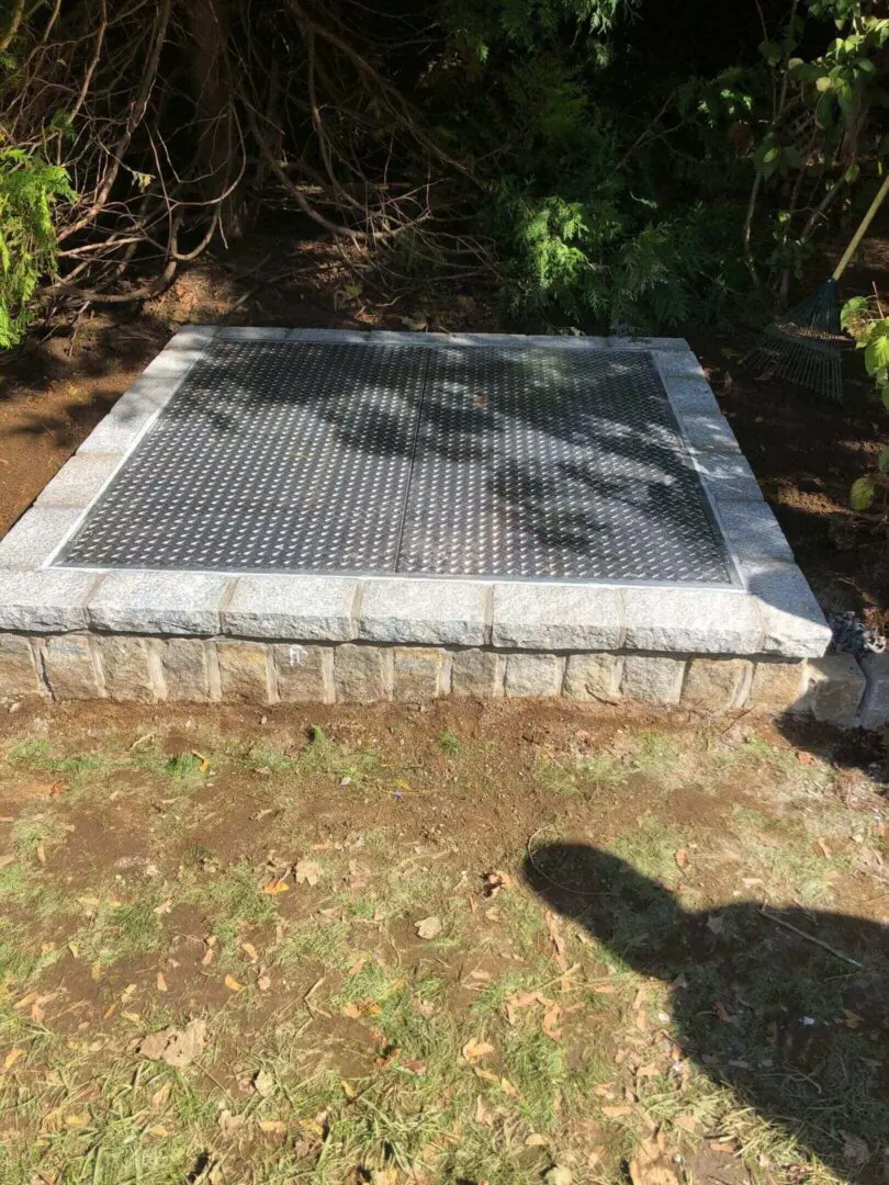 A square metal grate embedded in a stone frame outdoors.