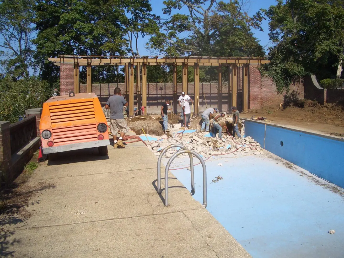 People enjoying a sunny day by an empty swimming pool.