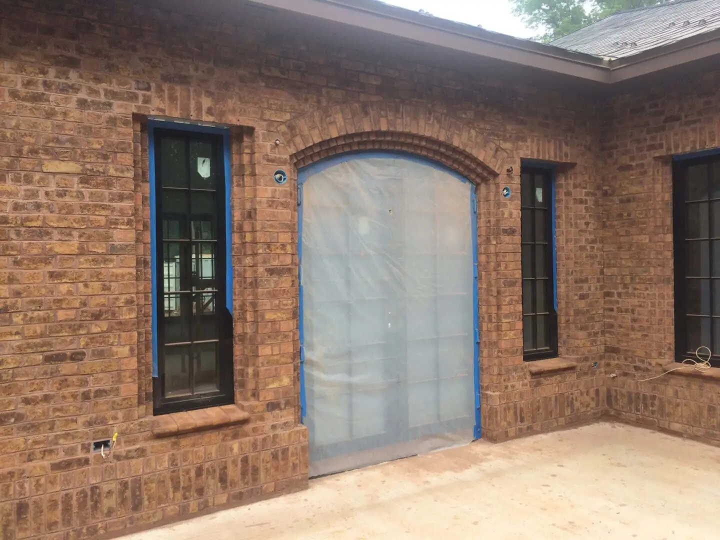 Brick house wall with two narrow windows and a covered arched doorway.