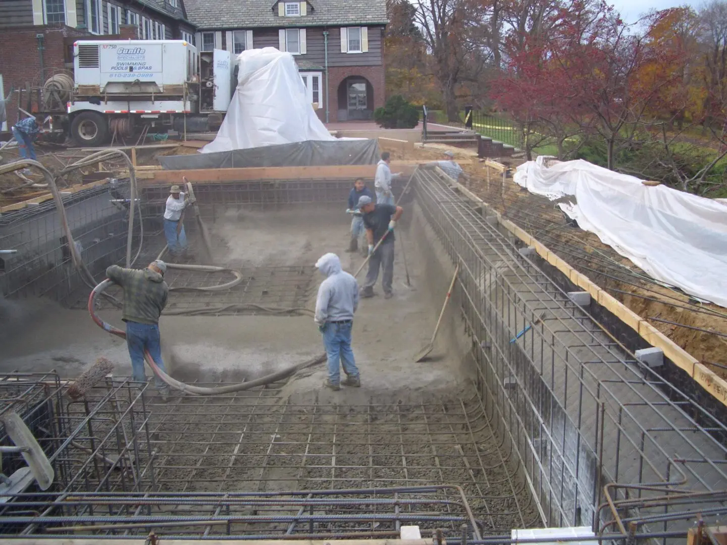 Workers preparing a pool foundation with concrete and steel reinforcement.