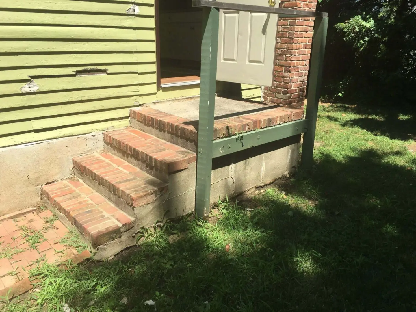 Outdoor brick steps with a green railing beside a house.