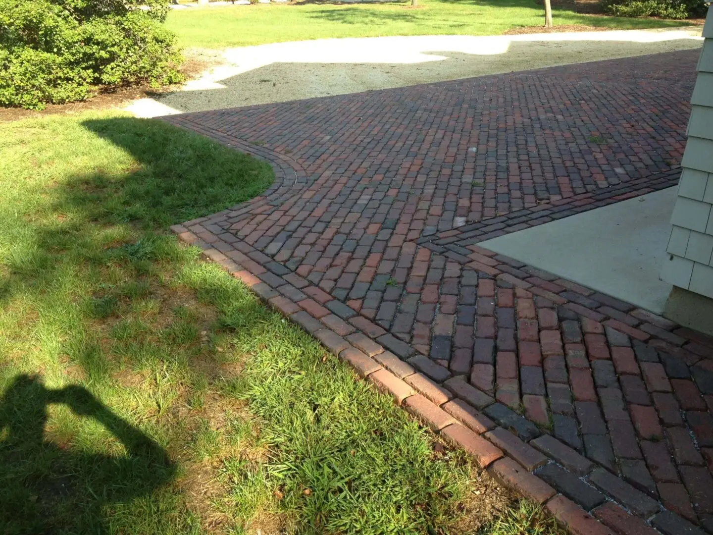 Brick driveway bordered by green grass and a concrete edge.