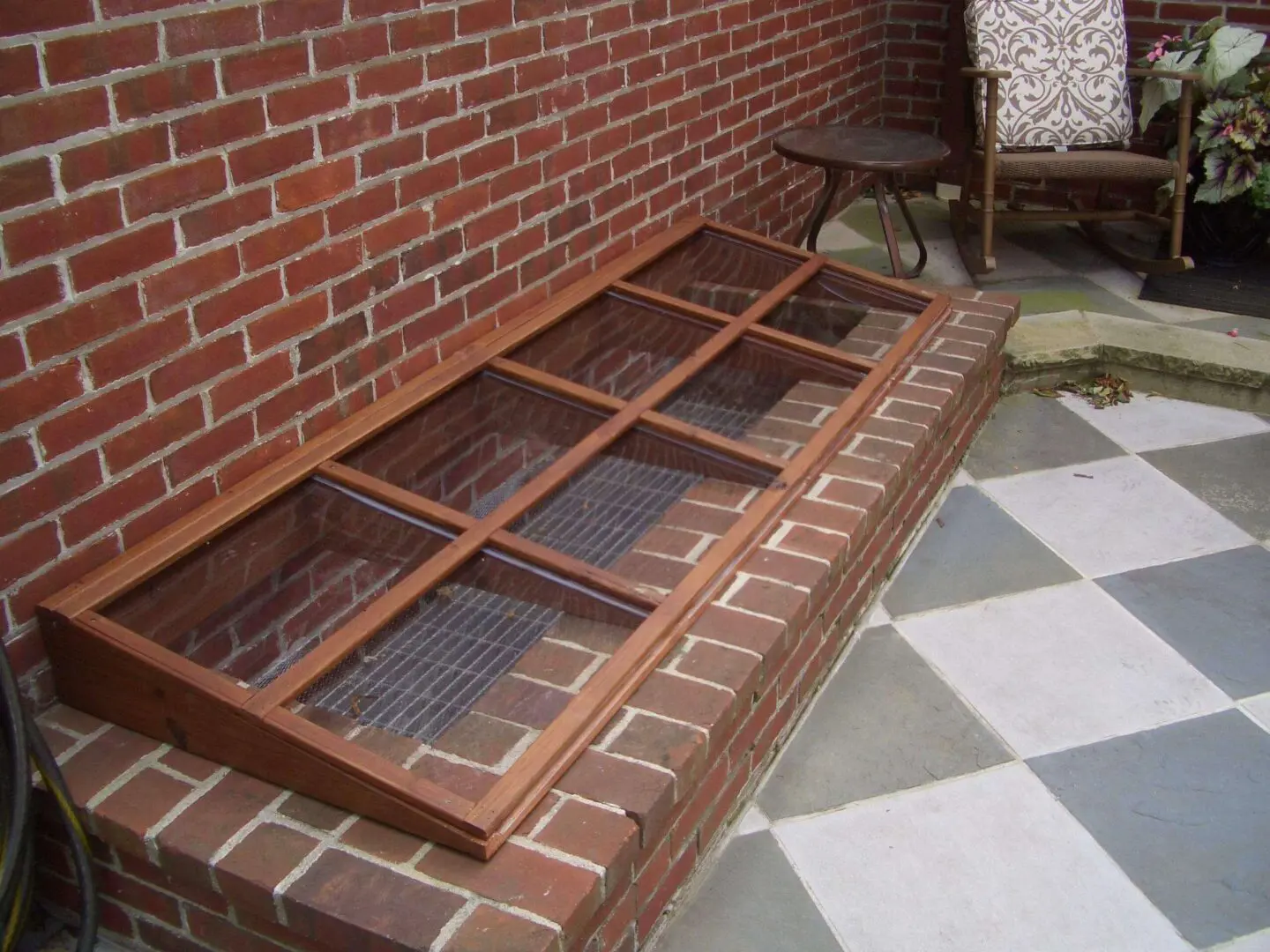 Brick cold frame garden bed with glass panels for plant protection.