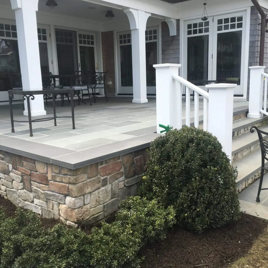 Elegant stone and wood porch with black metal furniture and green shrubs.