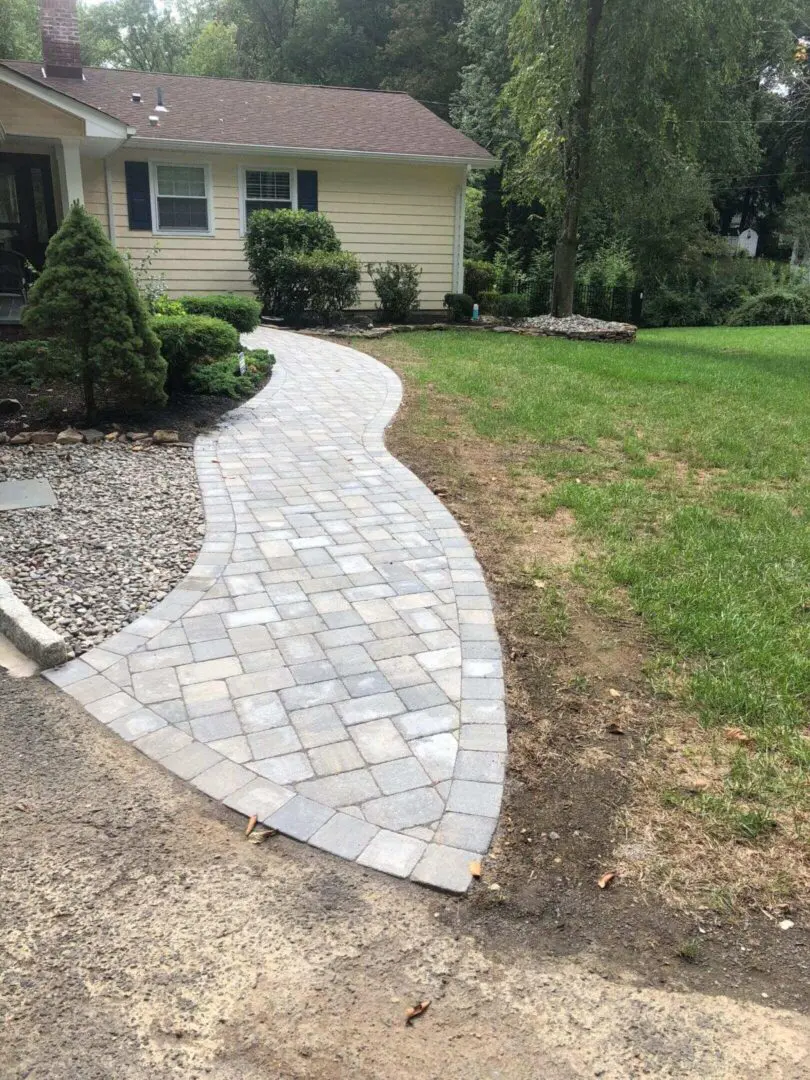Curved stone walkway leading to a house with green lawn and landscaping.