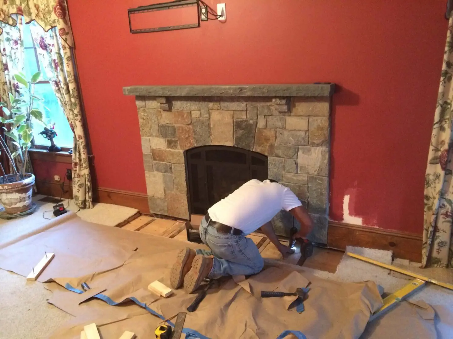 A man installs a stone fireplace in a red-walled room.