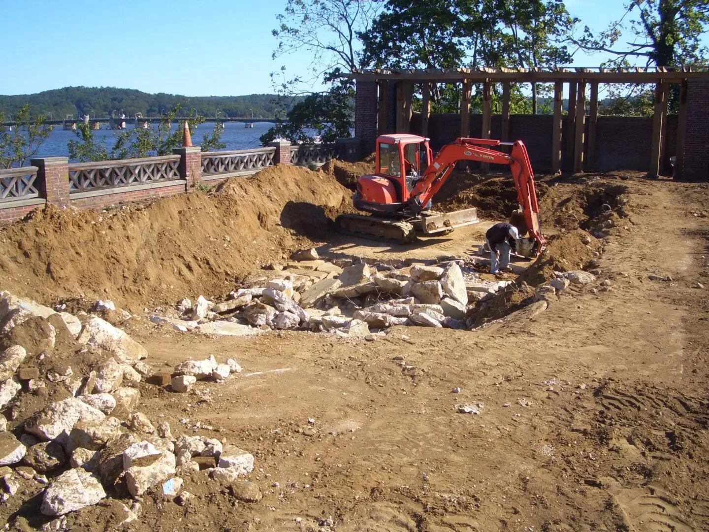 Excavator digging a large hole surrounded by dirt and rocks.