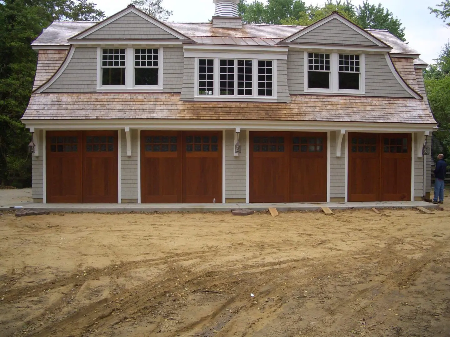 Newly constructed garage with four wooden doors and dormer windows above.