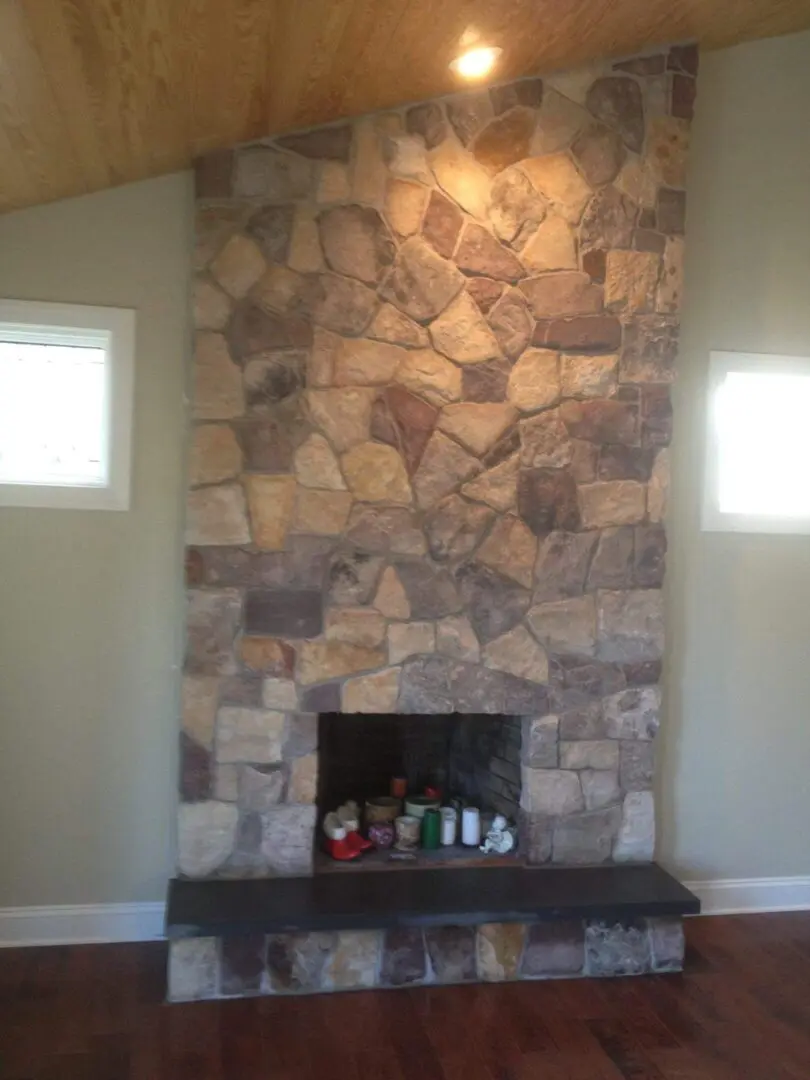 Stone fireplace with two small windows on either side in a cozy room.