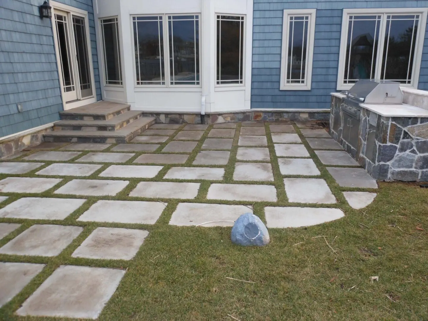 Backyard patio with stone slabs and grass patches.