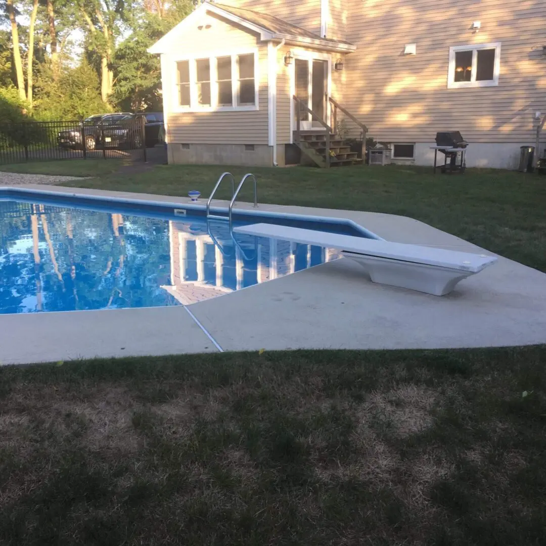 Backyard pool with a white diving board and green lawn.