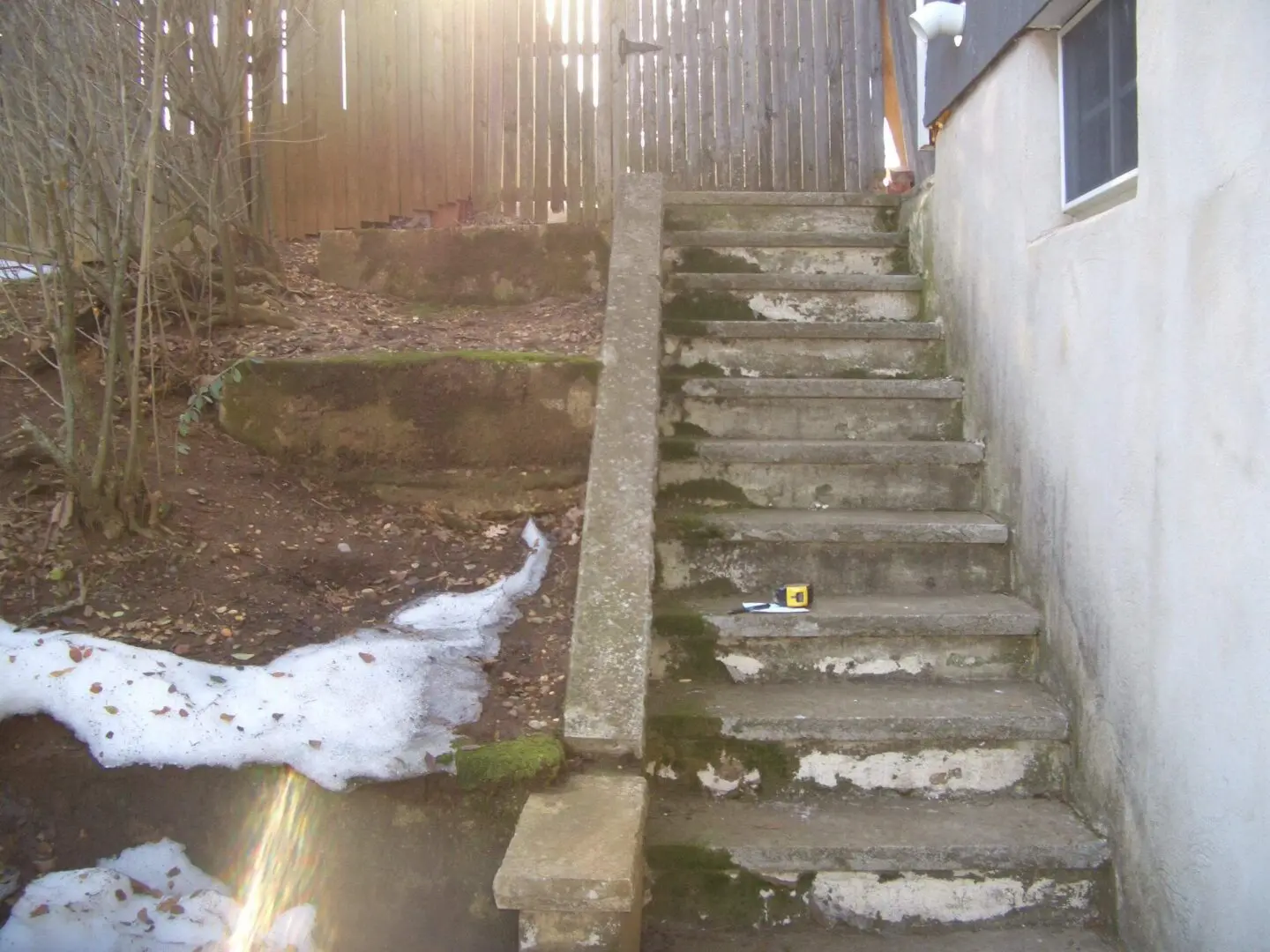 Old concrete steps with moss and remnants of snow beside them.
