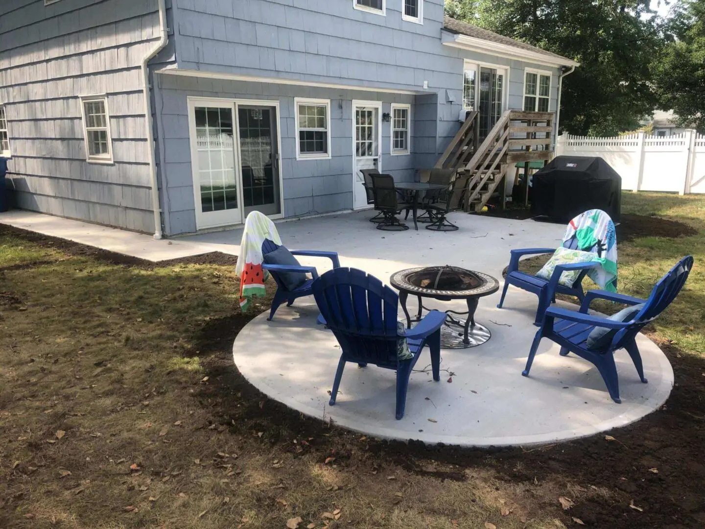 Backyard patio with blue chairs and a fire pit on a concrete slab.