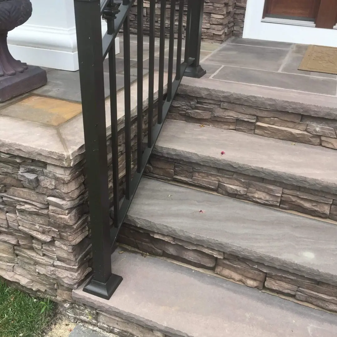 Stone steps with a metal railing and stone wall beside a front door.