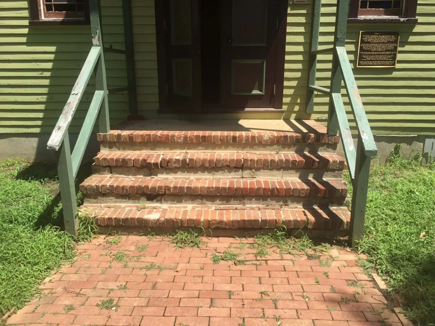 Brick steps and a walkway leading to a wooden porch with green railings.