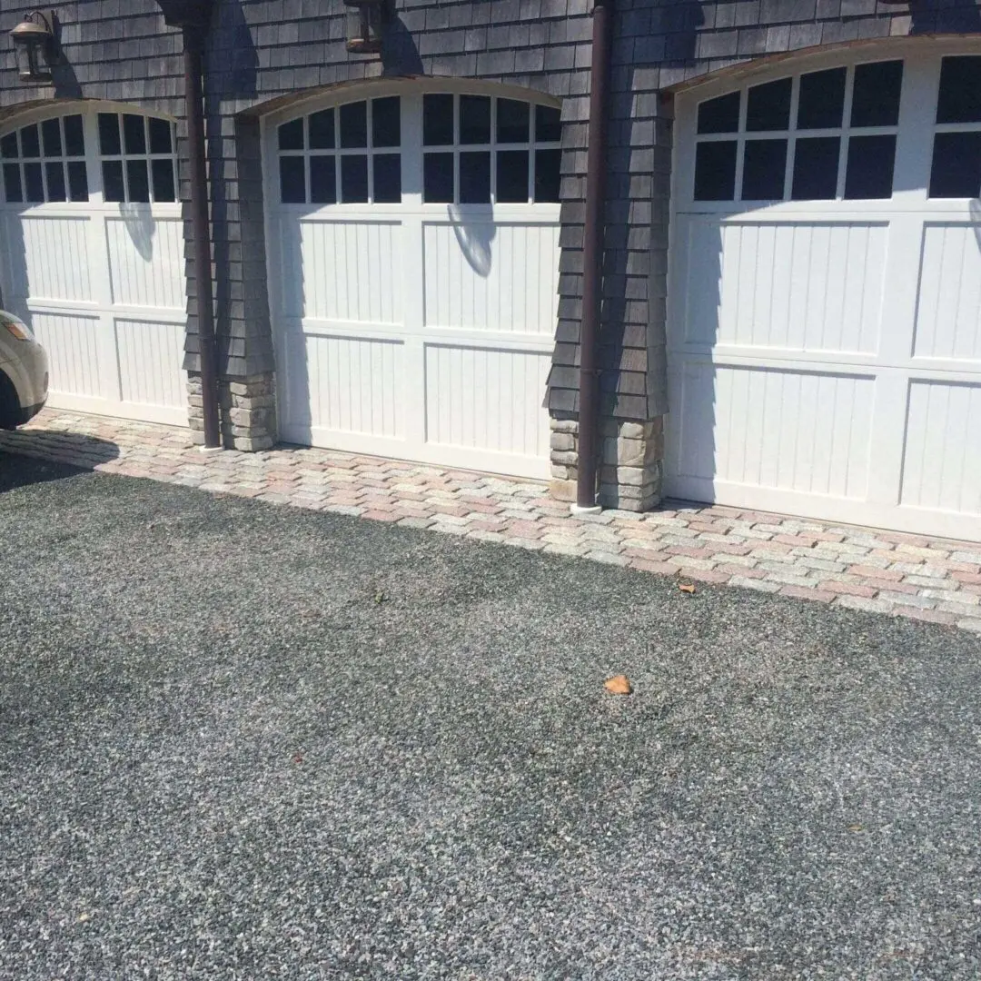 Two white garage doors with stone accents and a paved driveway.
