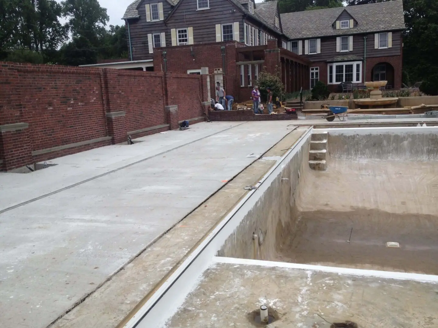 Newly poured concrete patio beside an empty pool in a residential backyard.