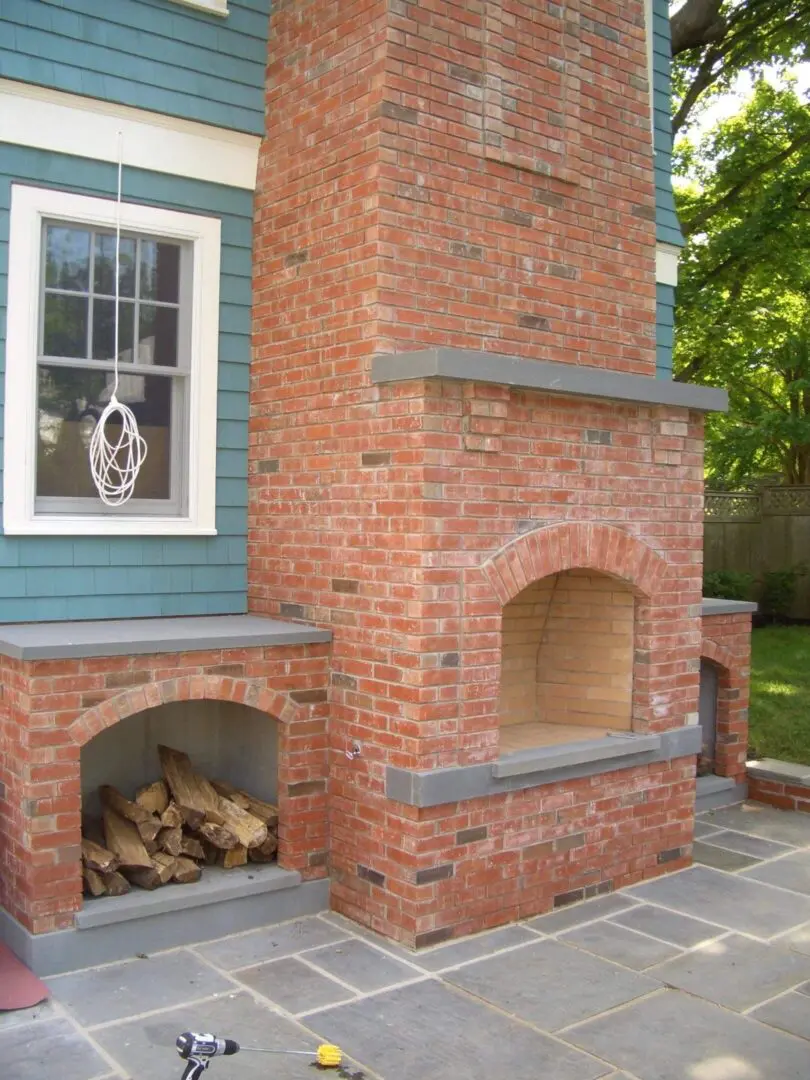 Outdoor brick fireplace with wood storage beneath a window.