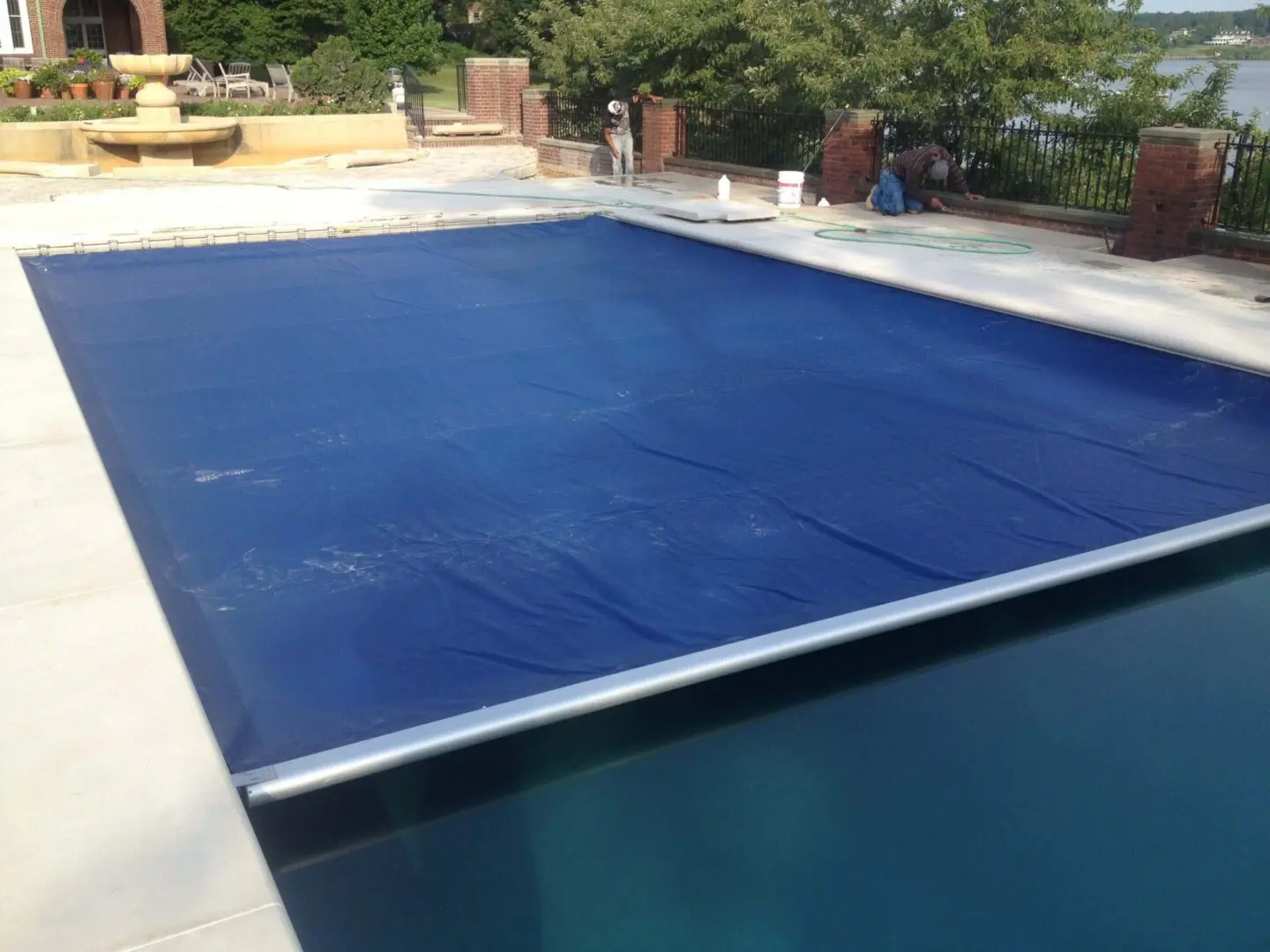 A swimming pool with a blue safety cover partially rolled out.
