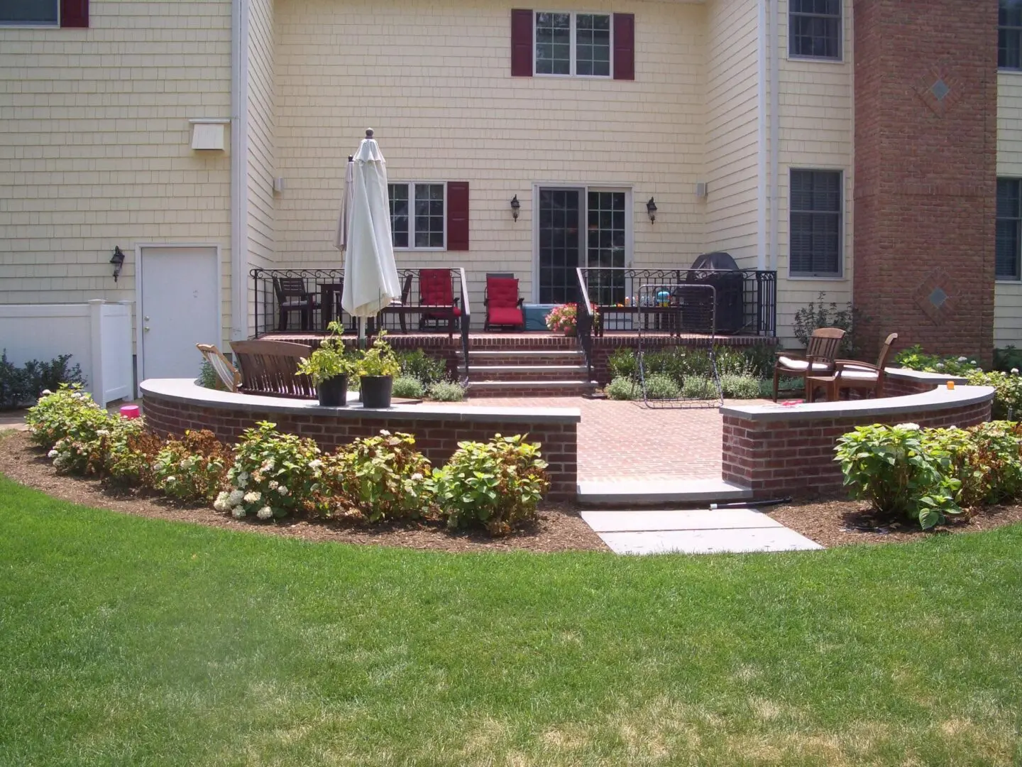 Backyard patio with seating, plants, and a green lawn.