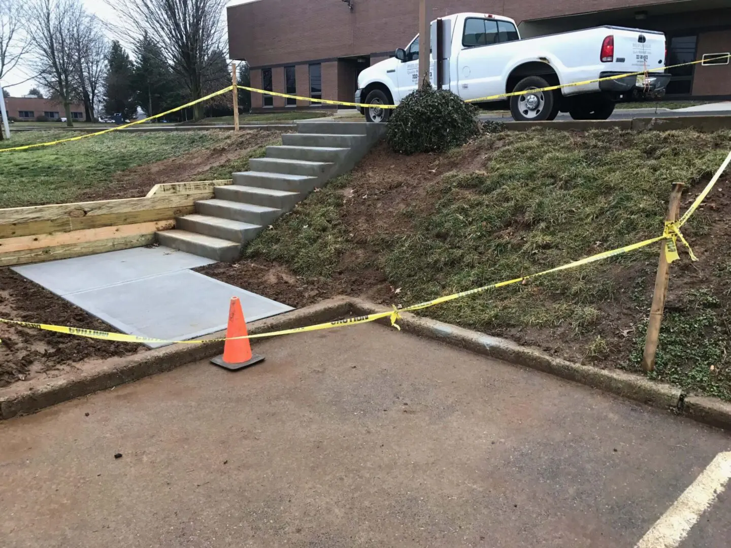 Newly poured concrete driveway and stairs with caution tape and cone around.