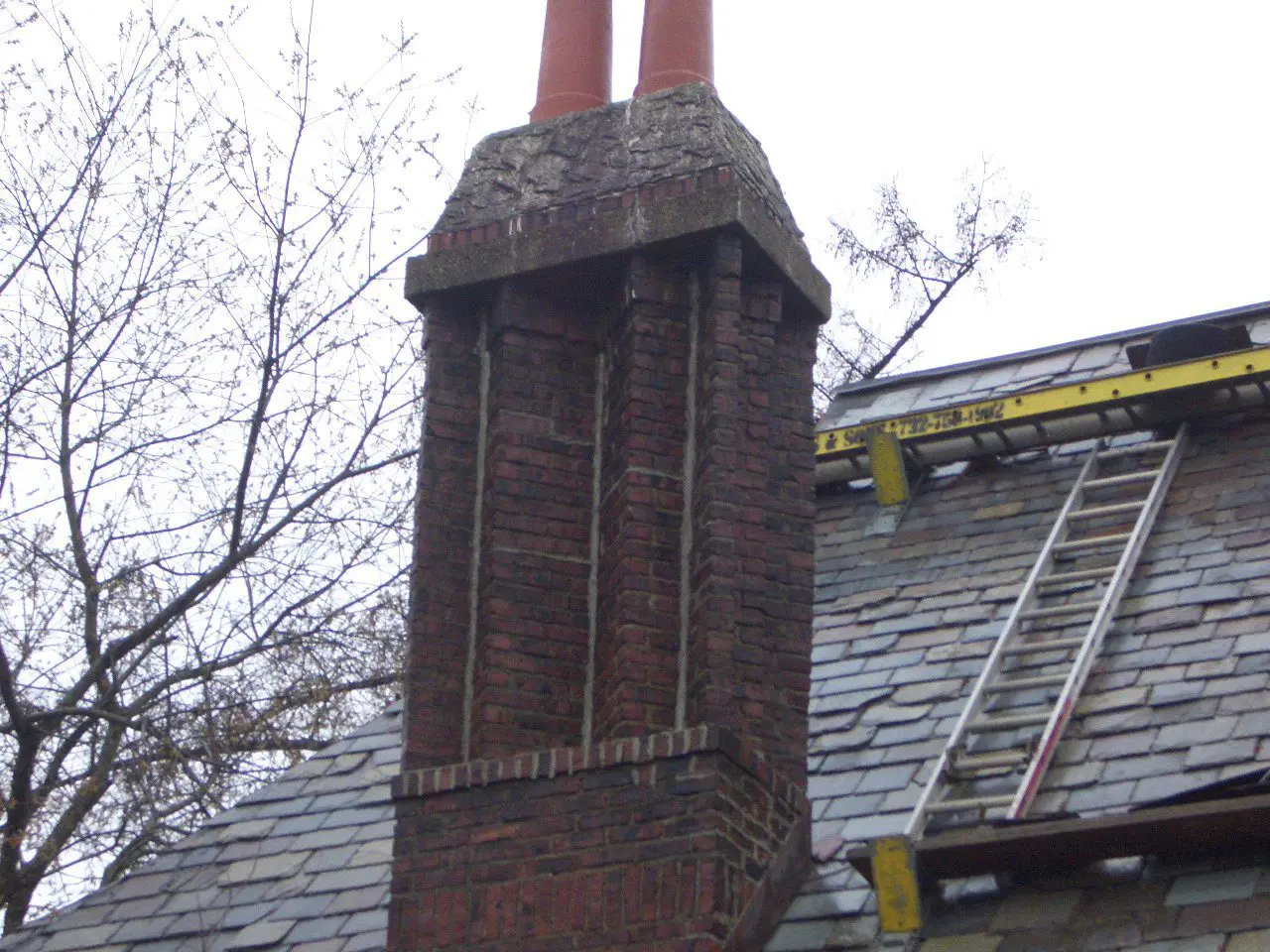 Close-up of a tall, red brick chimney with two terracotta pots.