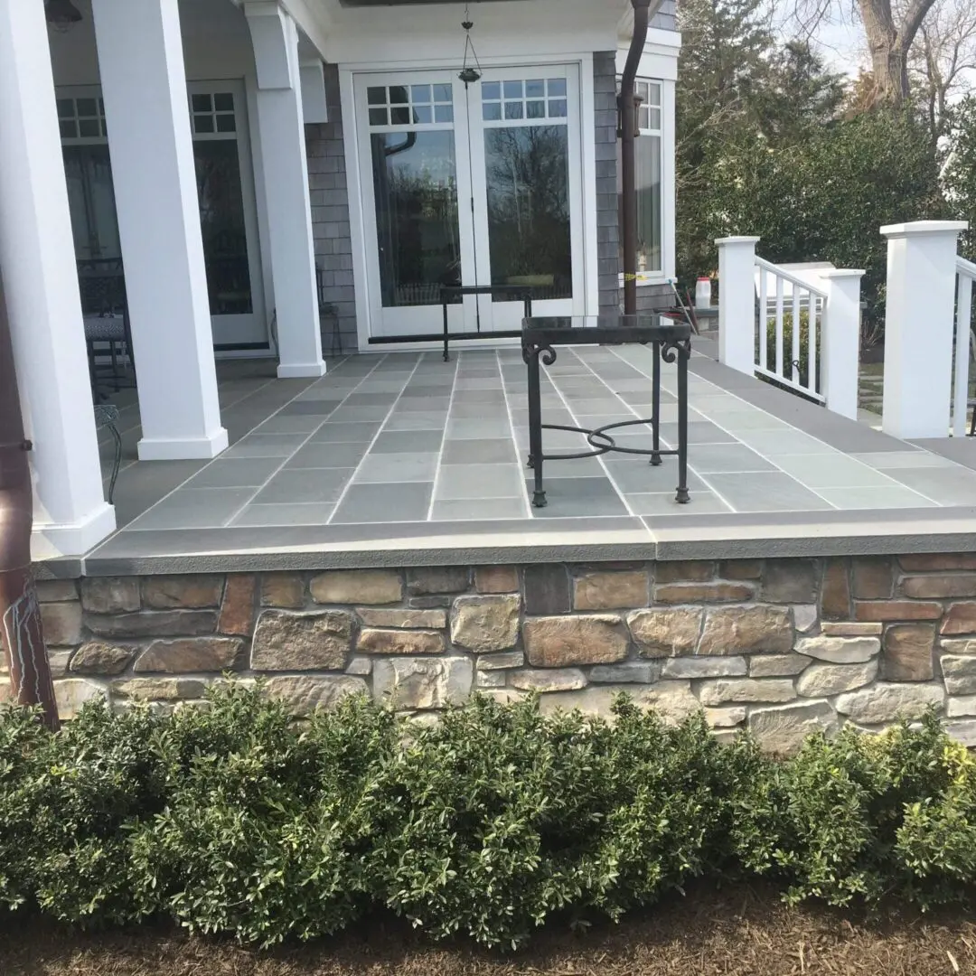 Empty rocking chair on a spacious stone porch with white columns.