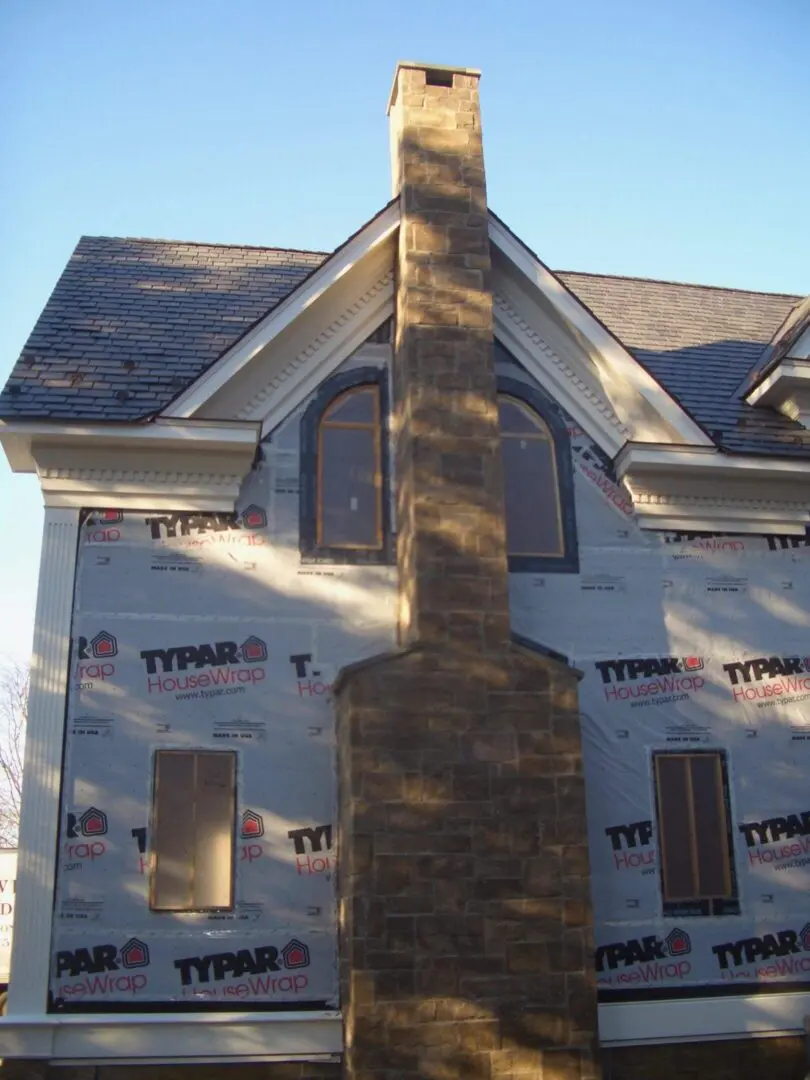 A house under construction with Tyvek building wrap and a stone chimney.