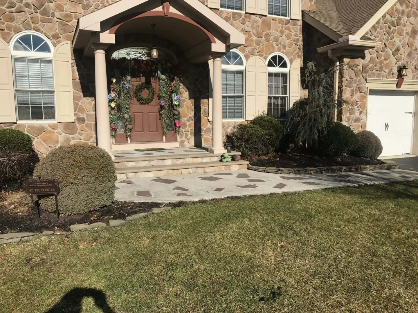 A stone pathway leads to a house entrance with double wooden doors and a decorative wreath.