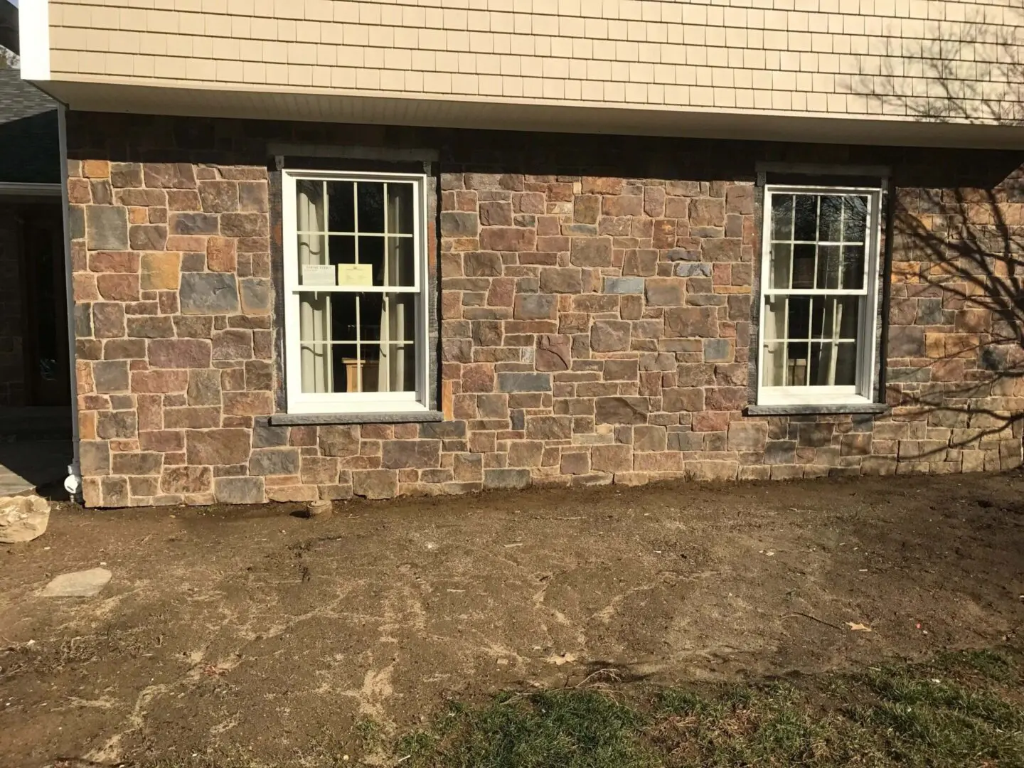 Two white-framed windows set in a stone brick wall with a patch of dry grass below.