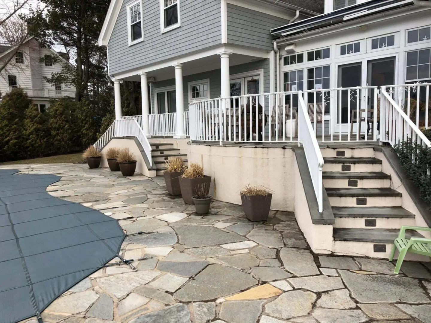Stone patio with steps leading to a house and a covered pool.
