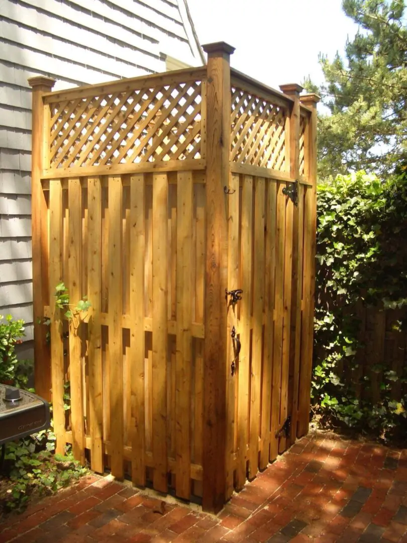 Outdoor wooden shower enclosure with lattice top in a garden.
