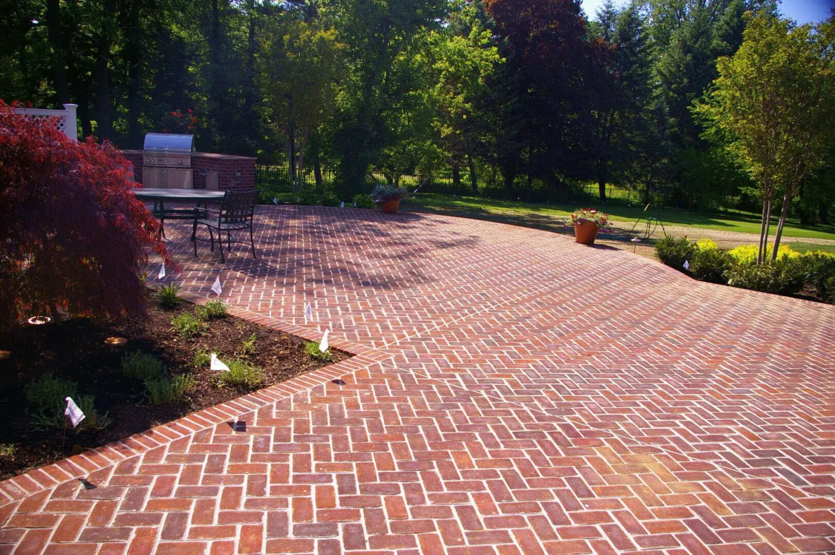 A red brick patio with a herringbone pattern surrounded by greenery.