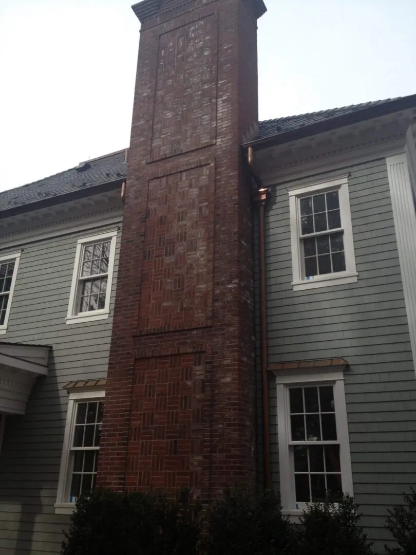 Tall brick chimney attached to a gray wooden house.