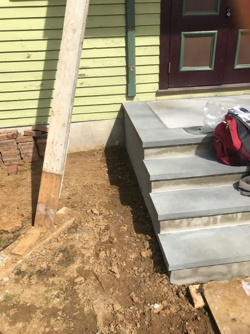 Concrete steps leading to a green wooden house with a dirt patch beside them.