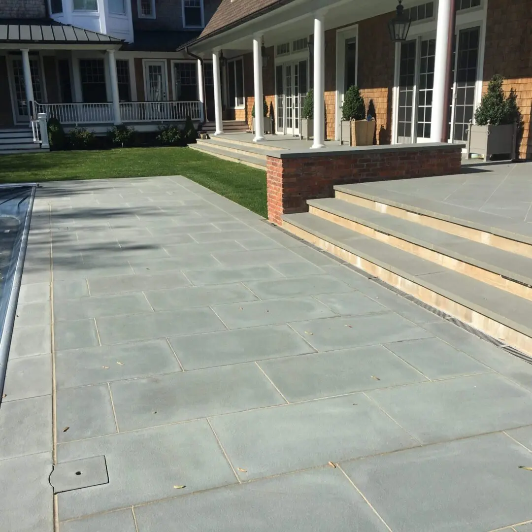 Modern backyard with stone patio and wooden steps leading to a porch.