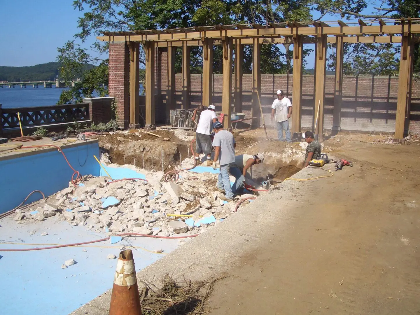 Workers renovating a pool area with tile removal underway.
