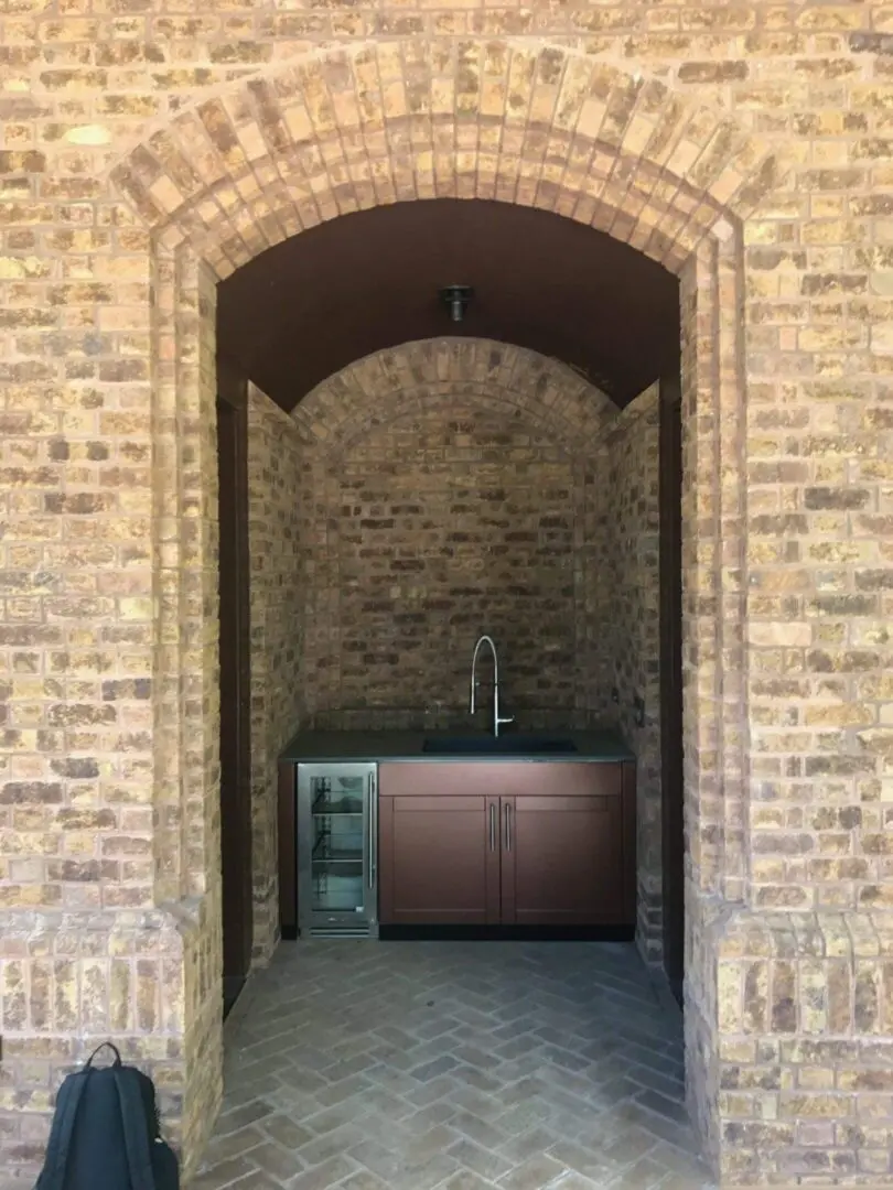 Outdoor kitchen nook with brick walls and a wooden cabinet under an archway.