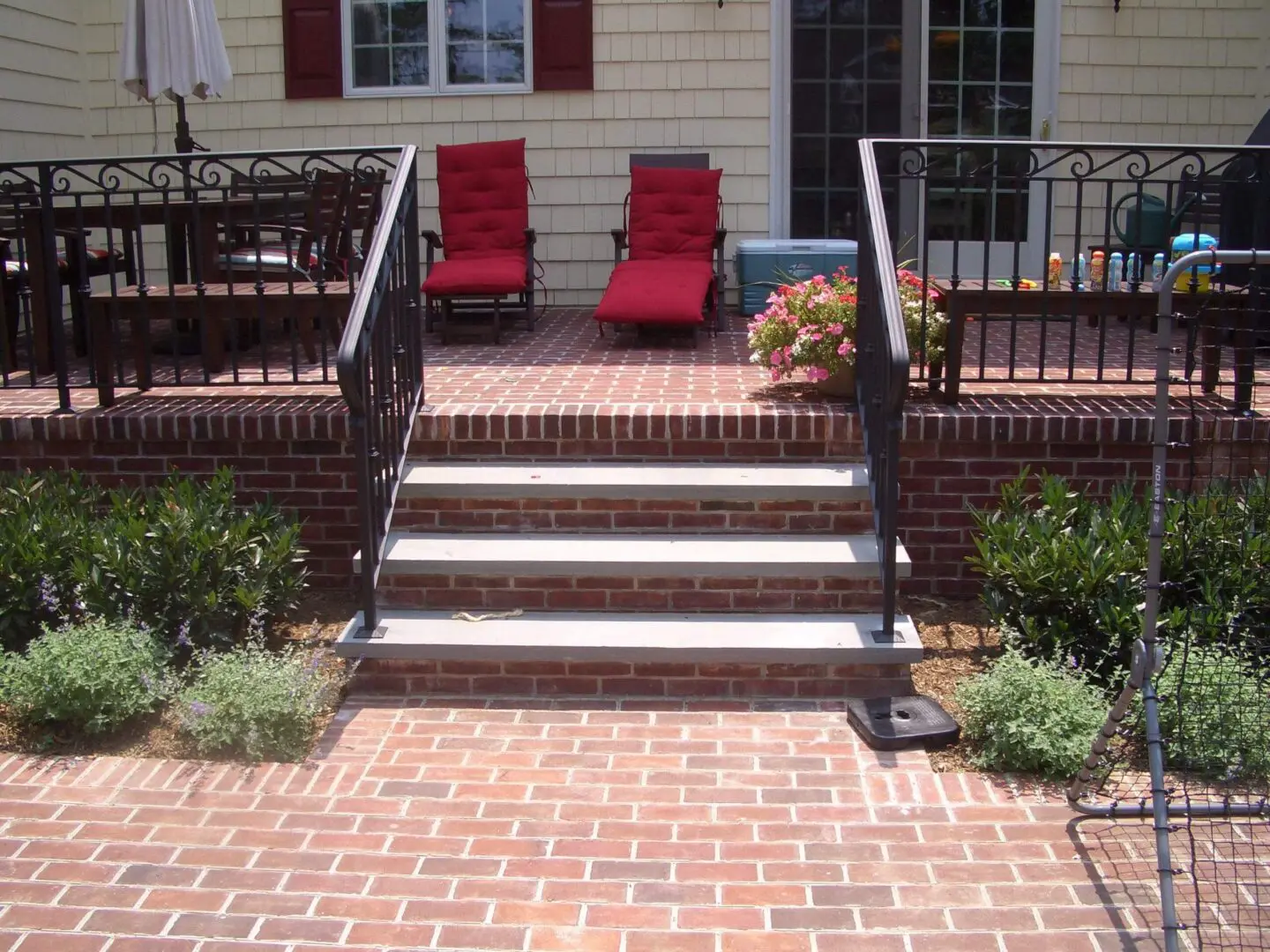 Brick stairs with black iron railings leading to a patio with red chairs.