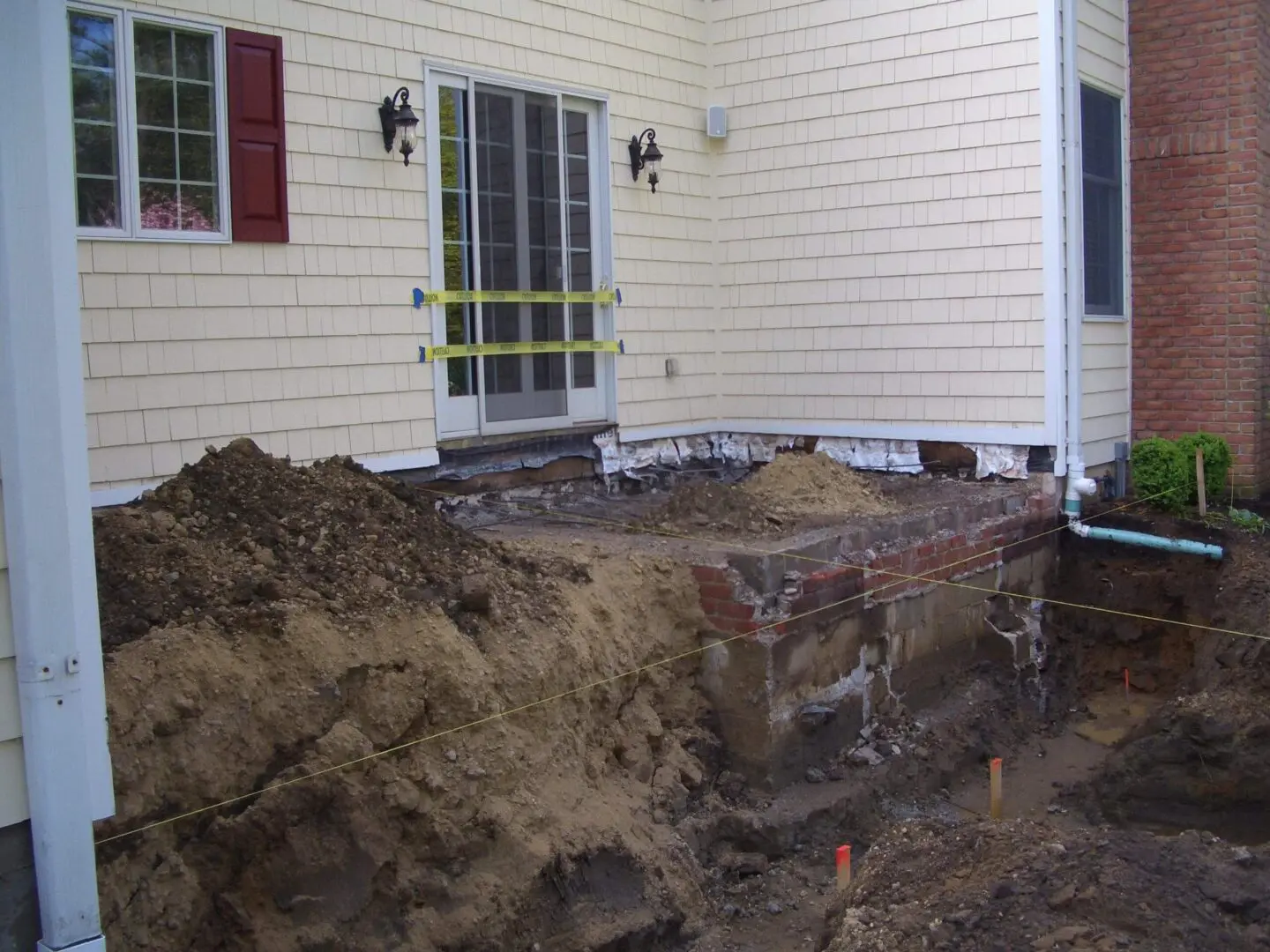 Construction site with exposed foundation and dirt pile beside a house.