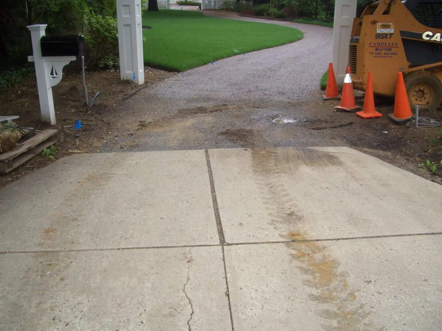 Concrete driveway with visible tire tracks and orange safety cones nearby.